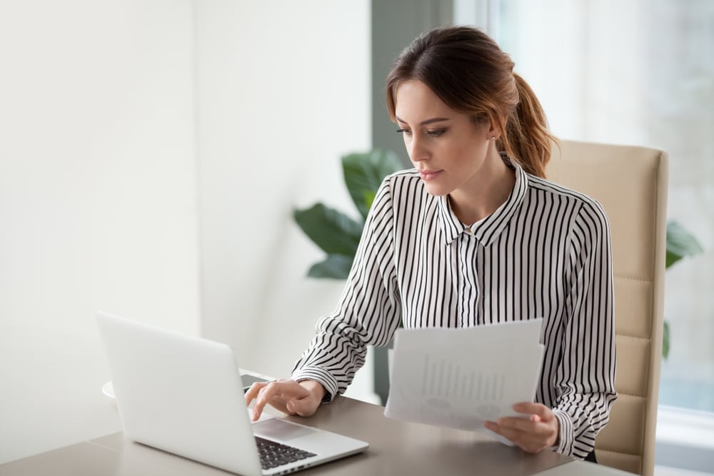 Woman organizing documents and searching for more on laptop