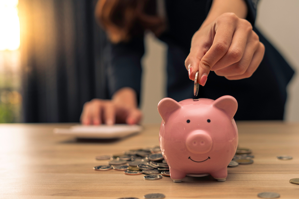 Woman putting coin in pink piggy bank