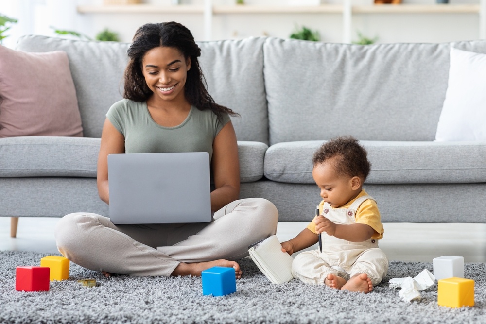 Mother working on laptop while child plays nearby