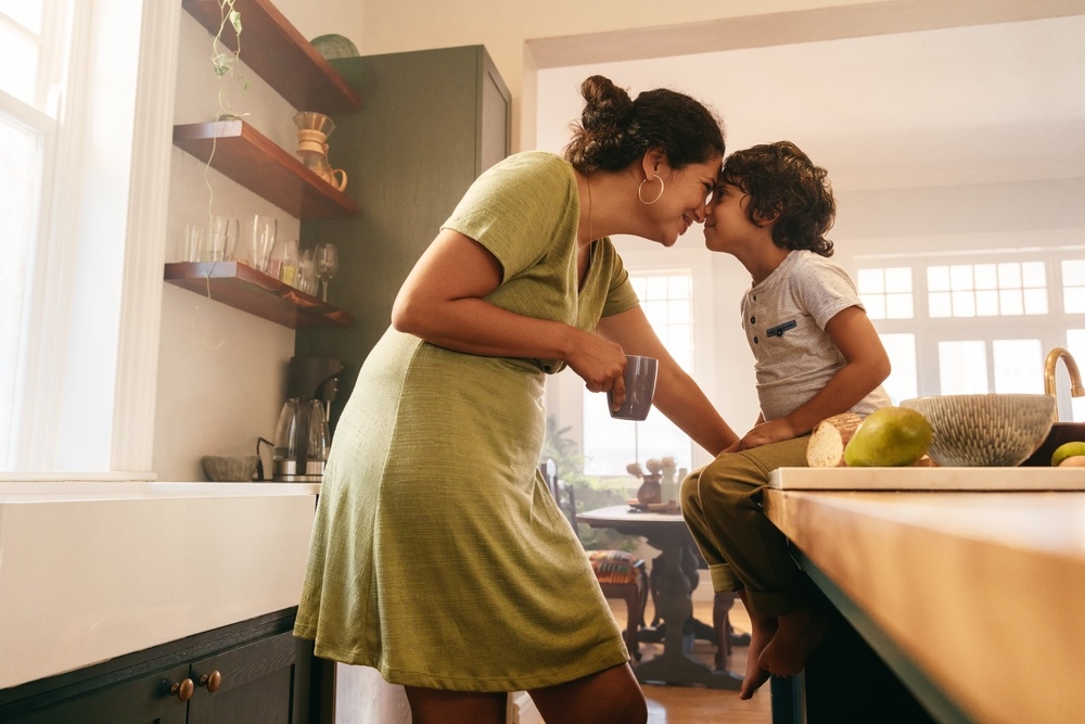 Affectionate mother touching noses with her young son in the kitchen. 