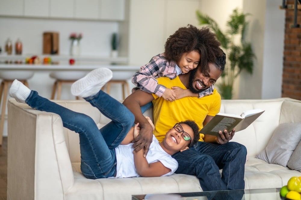 Dad reading book playing with daughter and son