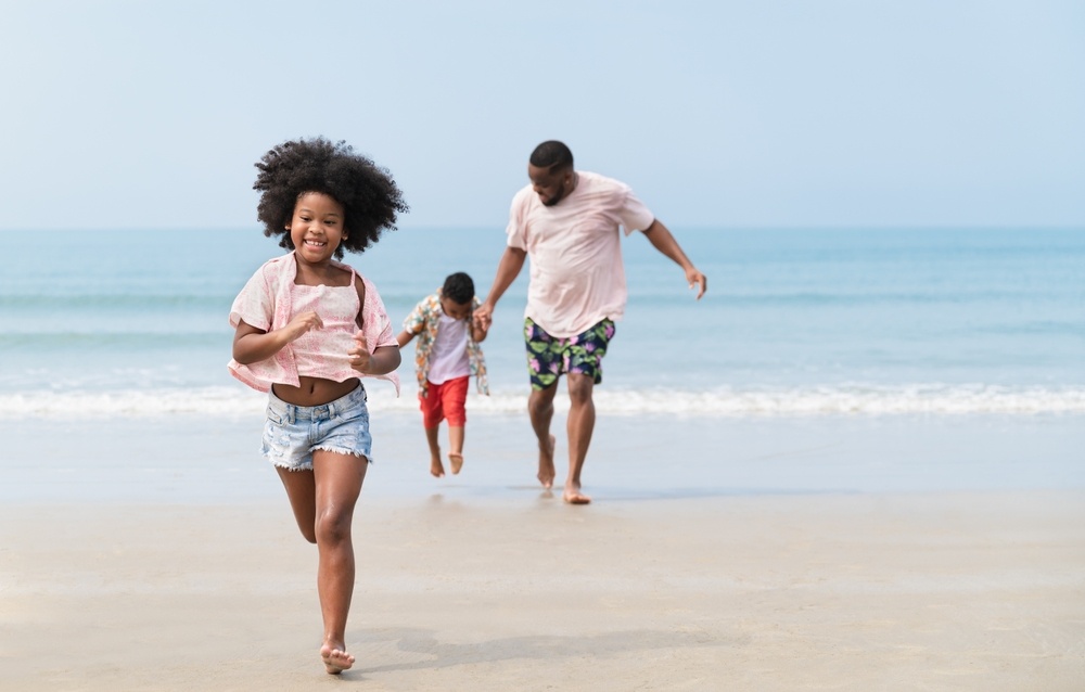 Happy African American kid girl run with family on the beach