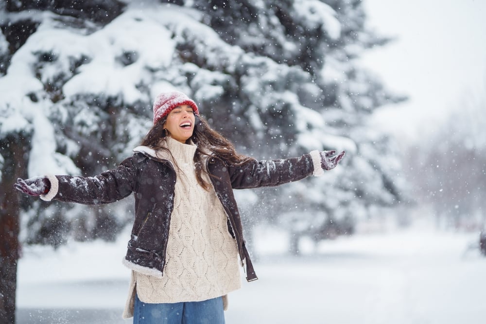 Woman standing in snow with arms spread wide embracing life