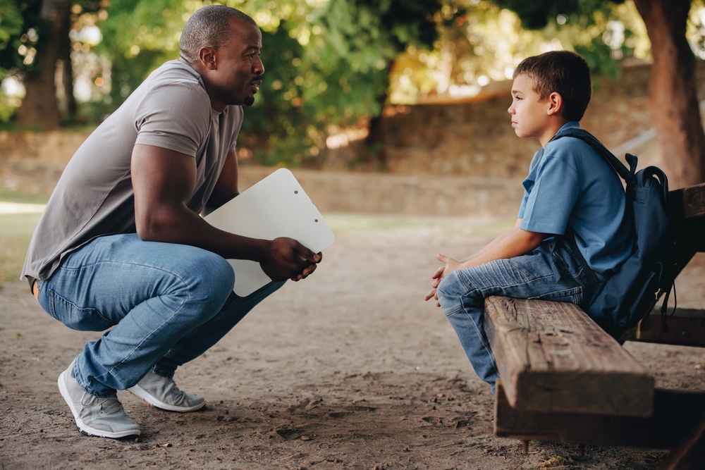 School teacher motivating a young primary school kid outside class. Child mentor talking to a troubled school boy. Support and encouragement for a student in elementary school.