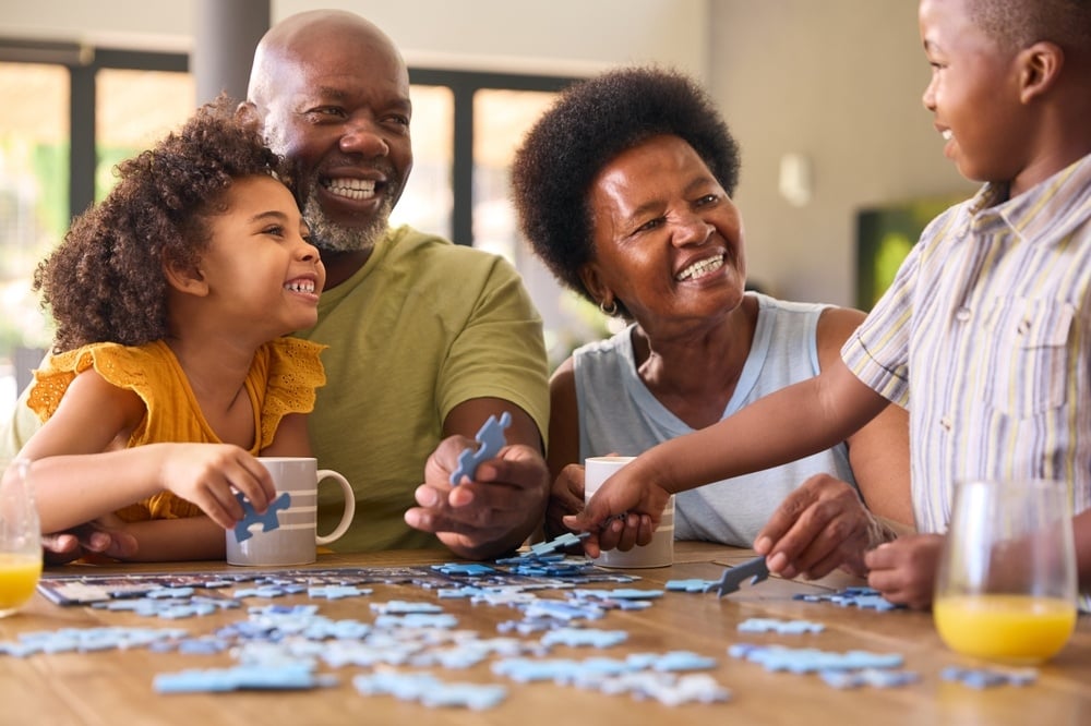 Family Shot With Grandparents And Grandchildren Doing Jigsaw Puzzle On Table At Home