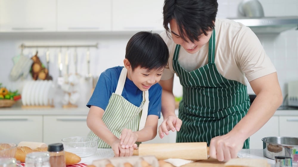 Asian single father teaching son how to use a rolling pin for cooking 