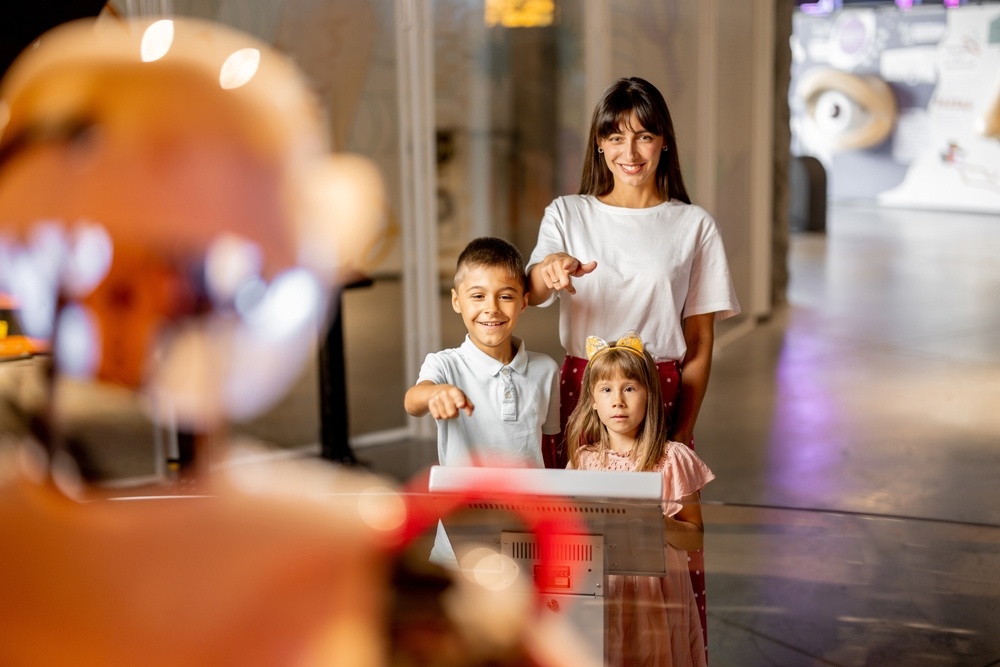 Mom with kids are excited to interact with a robot, visiting together science museum. 