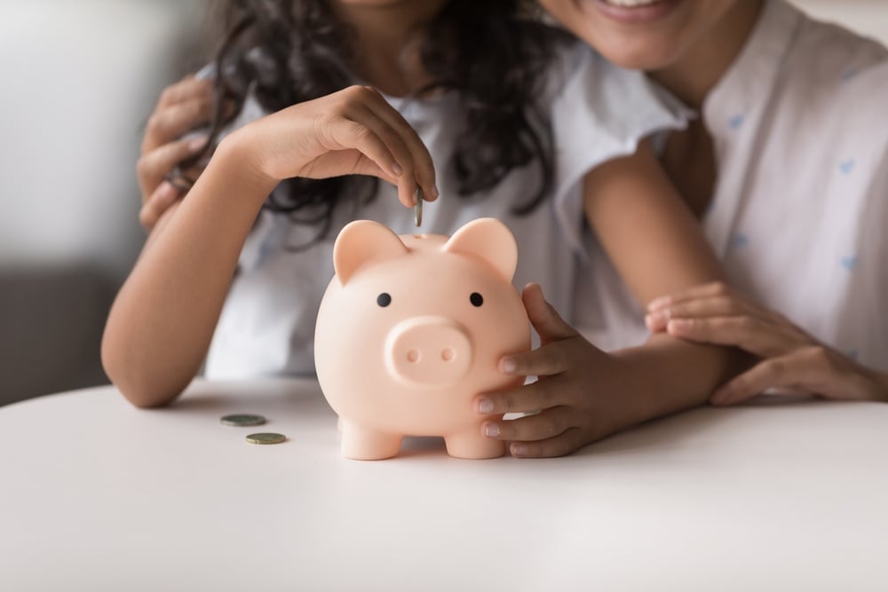 Little girl put coin into piggy bank, caring of family budget with mother, close up crop shot. Savings management, money investment, save finances, planning future for purchases or insurance concept