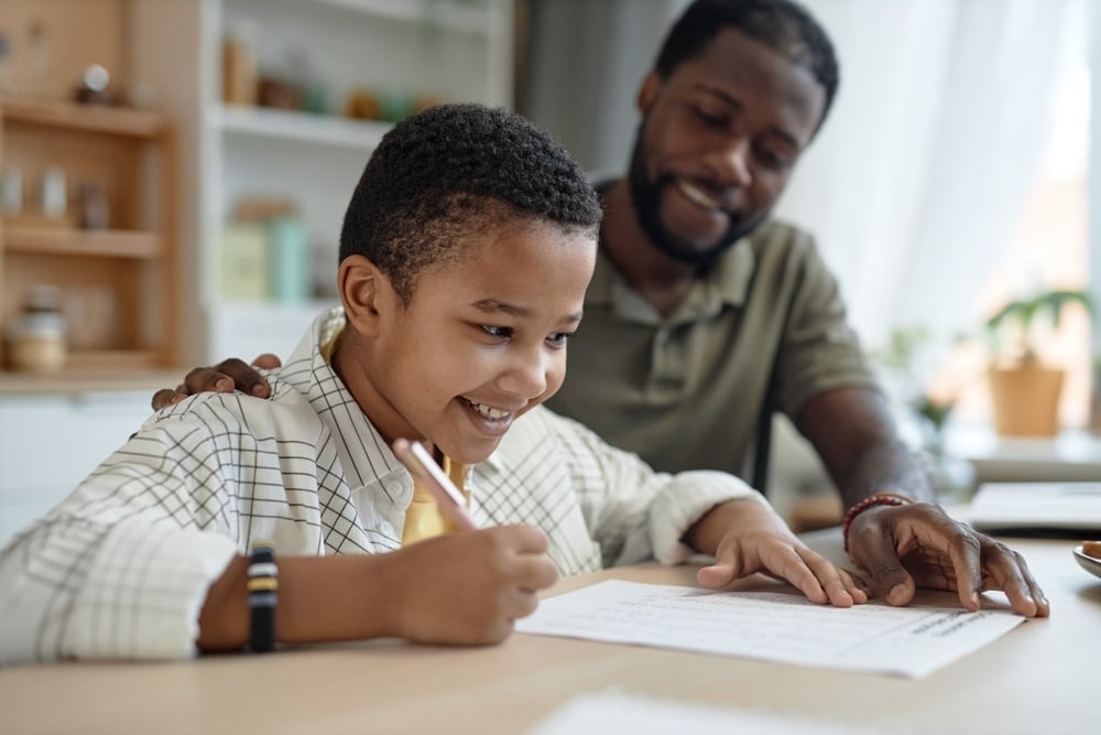 Portrait of happy African American boy doing homework at kitchen table with supportive father