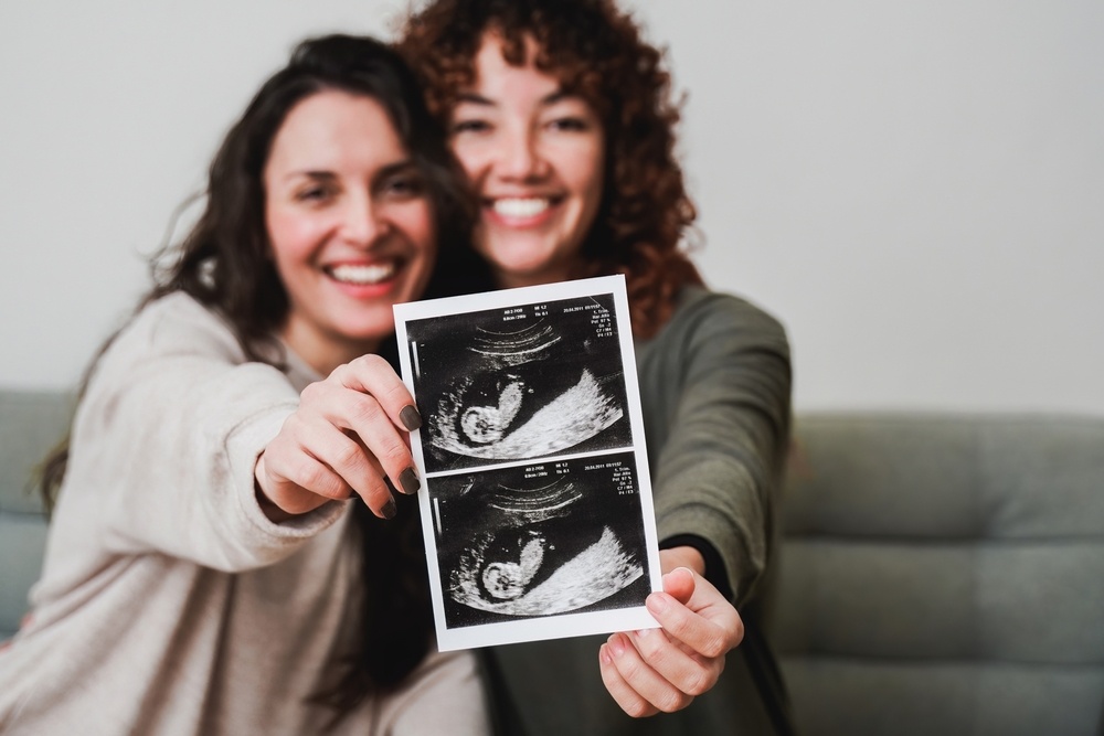 Happy LGBTQ+ couple holding ultrasound photo scan at home