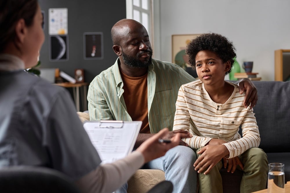 Portrait of teenage boy listening to psychologist during family therapy session with caring father