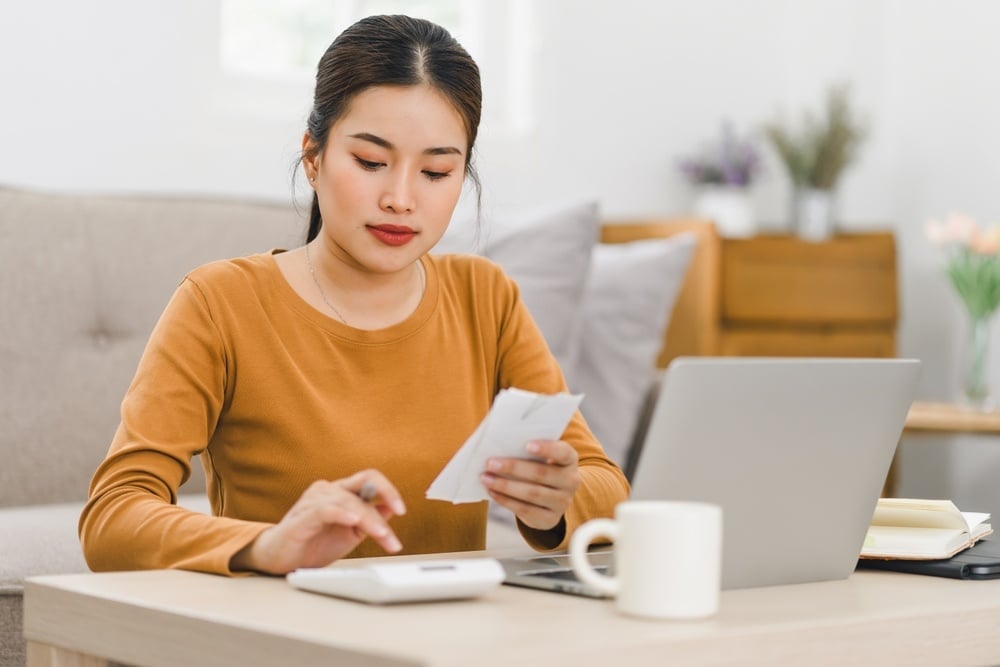 Focused woman calculating expenses using calculator and laptop at home, managing finances